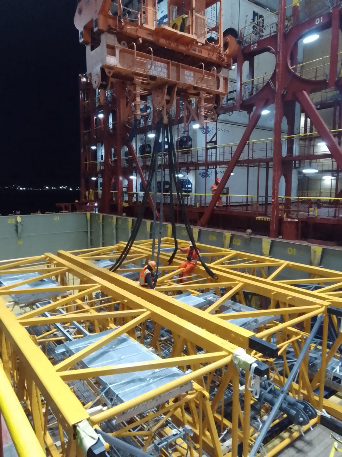 Riggers guiding a suspended steel truss into a cargo hold