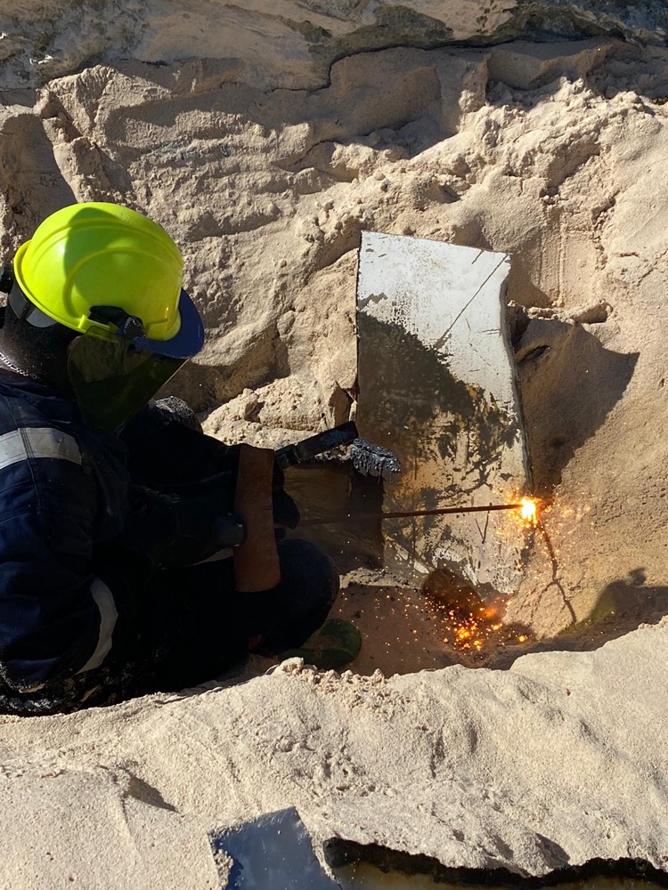 OEM Bahamas crew cutting embedded metal wreckage from shoreline rock
